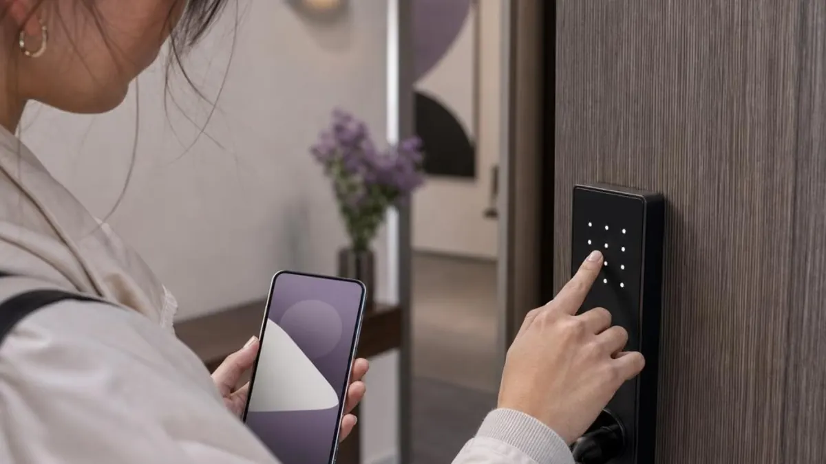 Guest entering a code on an apartment’s smart lock, holding a mobile phone in the other hand
