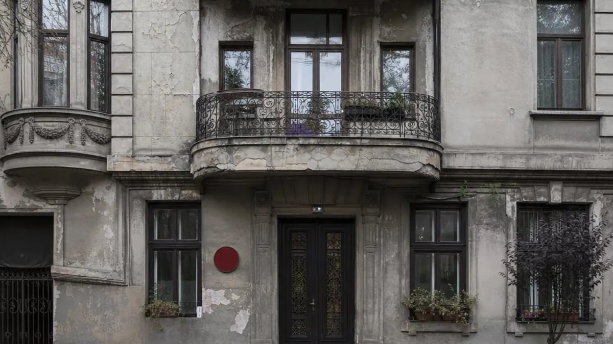 Facade of an old Bucharest building with a wrought-iron balcony and a red seismic-risk dot next to the entrance