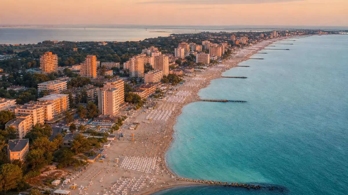Aerial view at sunset of a seaside resort with tall hotels, a beach lined with sun loungers and breakwaters in the sea